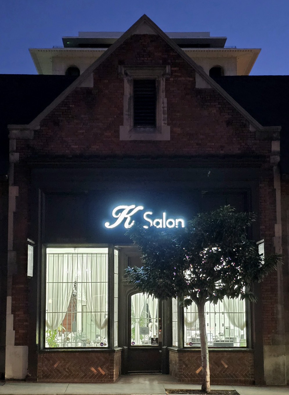 The K Salon shopfront on West 6th Street at dusk, with the illuminated script sign above the windows